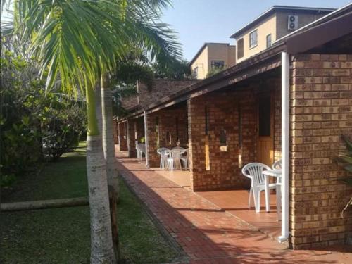 a patio with white chairs and tables and a palm tree at Flamboyant Apartments in St Lucia