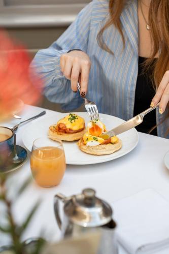 a woman eating pancakes on a plate with a fork and knife at Feversham Arms Hotel & Verbena Spa in Helmsley