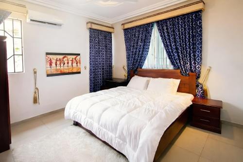 a bedroom with a large bed and blue curtains at Aduk Guest House Airport City Accra in Otele