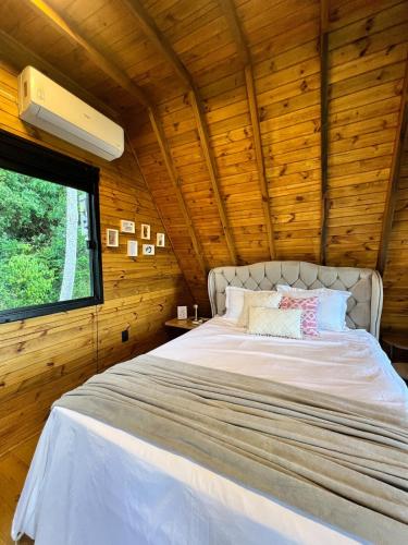 a bed in a wooden room with a window at Chalé Sol Nascente - Vista espetacular próximo as melhores praias de Floripa in Florianópolis