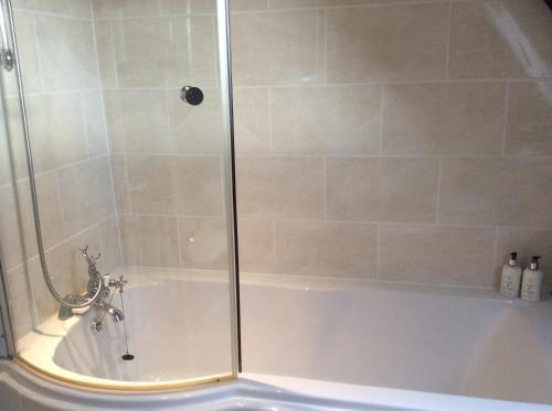 a shower with a glass door on a tub at Castle Farm House B&B in Corby