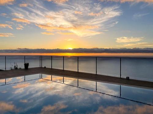 a reflection of the sun in the water with a dock at Valley View-Villa with heated pool and sauna in Arco da Calheta