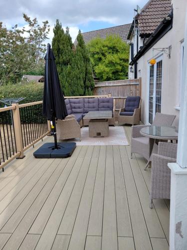 a patio with an umbrella and furniture on a deck at Spacious family cottage with private garden and forest walks in Burley