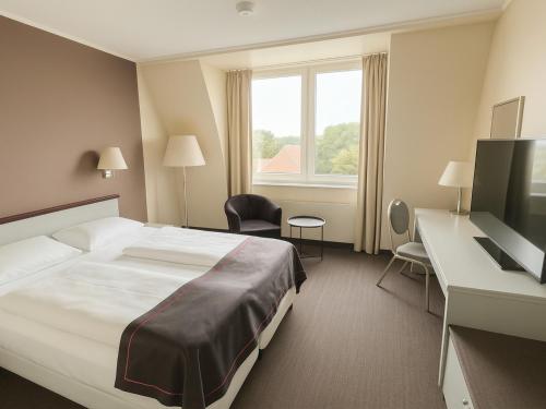 a hotel room with a bed and a desk and a television at DORMERO Hotel Dessau-Roßlau in Dessau