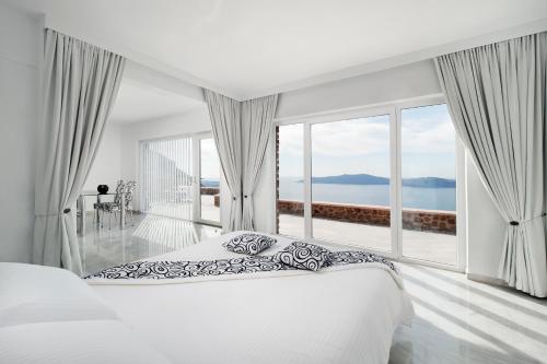 a white bedroom with a bed and large windows at Anastasis Apartments and Spa in Imerovigli