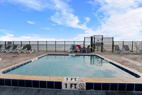 a pool on a patio with chairs and a fence at Outrigger Beach Club Resort by CoolVacay in Ormond Beach