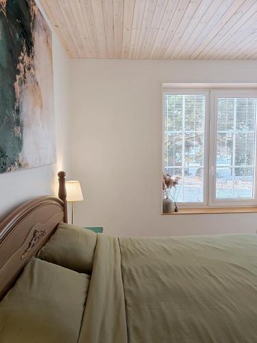 a white bedroom with a bed and a window at Pievų Tako kiemelis in Klaipėda