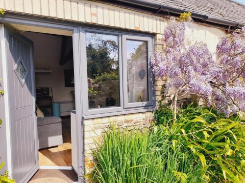 an open door to a garden with purple flowers at Forge Cottage, Cosy Couples Retreat in the Devon Countryside, Indoor Pool, Tennis Court and Tarka Trail Access in Merton