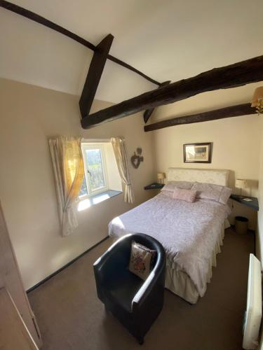 a bedroom with a bed and a chair and a window at Forge Cottage, Cosy Couples Retreat in the Devon Countryside, Indoor Pool, Tennis Court and Tarka Trail Access in Merton