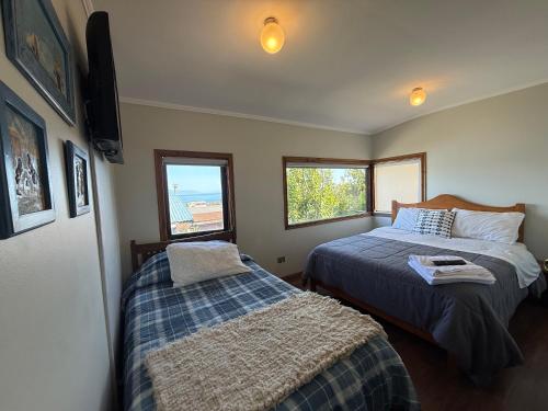 a bedroom with two beds and two windows at Hostal y Cabañas Mirando al Mar in Puerto Montt