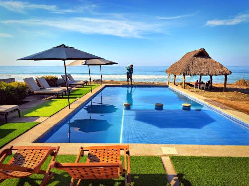 ein Swimmingpool mit Liegestühlen und einem Sonnenschirm und das Meer in der Unterkunft Brisa Bliss in San Juan de Alima