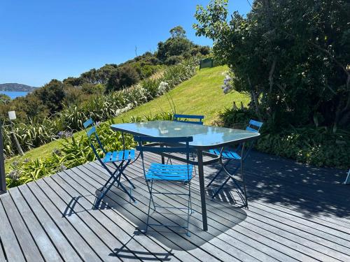 a table and chairs on a deck with a view of the water at Aroha A-Frames - Bush & Beach Retro Retreat in Coromandel Town