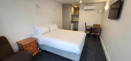 a small bedroom with a white bed and a chair at Waikato Hospital Motel in Hamilton