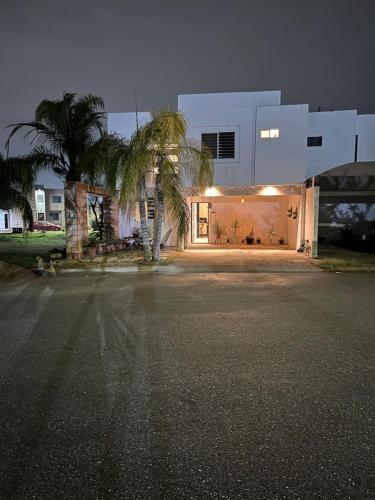 a white house with a palm tree in front of it at Casa completa, 4 dormitorios, 7 camas dobles, 3 sofá cama, 3 baños 1 en planta baja, cocina equipada, consola Arcade, asador, juguetes para niños, plancha, secadora, cafetera, etc, fraccionamiento privado, zona de vías rápidas y toallas in Torreón