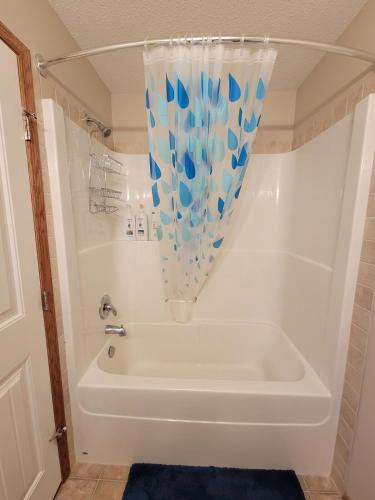 a white bath tub with a blue and white shower curtain at Quaint Lonsdale Suite in Red Deer