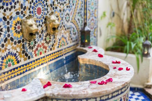 uma fonte com pétalas de rosa vermelhas numa parede de mosaico em Riad Jardin Chrifa em Fez