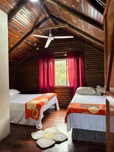 two beds in a room with red curtains at Cabaña Brisa Del Río in Cooper