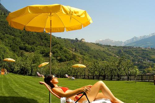 a woman sitting in a chair under an umbrella at Hotel Öhlerhof in Lagundo