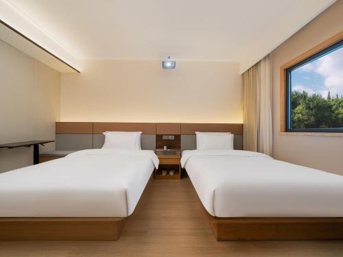 two beds in a room with a window at The Screen Hotel Hangzhou East St ation-Zhanongkou Metro in Hangzhou