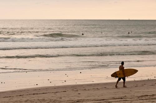 a man walking on the beach with a surfboard at Santa Teresa Surf Vista Villas in Santa Teresa Beach