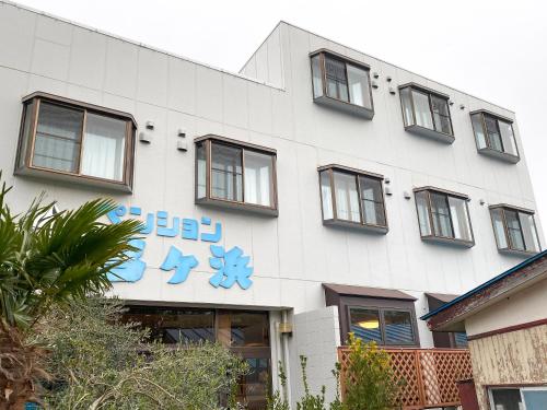 a white building with a blue sign on it at Pension Yumigahama in Minamiizu