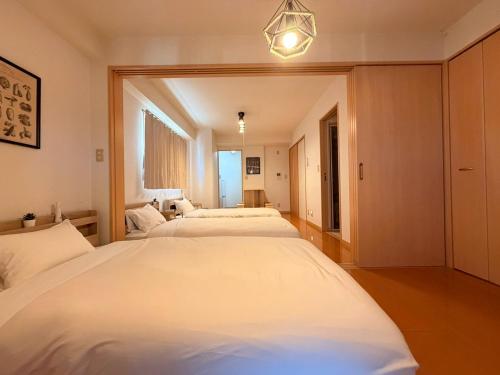 a bedroom with three white beds and a chandelier at ura アオトハル2 in Okayama