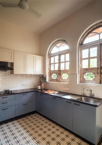 a kitchen with white cabinets and a sink and two windows at LohonoStays Calisto Villa E in Camorlim