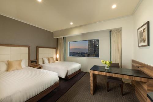 a hotel room with two beds and a desk and a window at Palace Hotel Omiya in Saitama