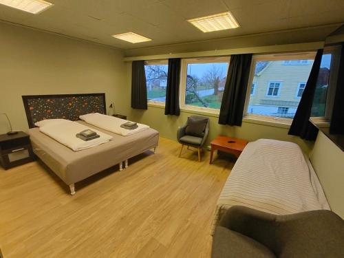 a bedroom with two beds and a chair and windows at Gjøa Motell in Rosendal