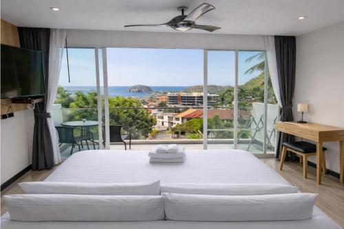 a bedroom with a large white bed and a large window at Santosa Hotel & Welness Center in Kata Beach