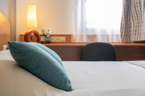 ein Bett mit einem blauen Kissen darauf in der Unterkunft Brit Hotel Bressuire in Bressuire
