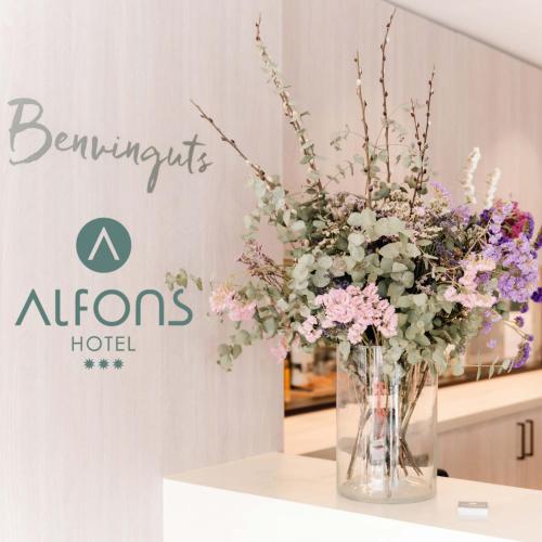 a vase of flowers on a table in front of a sign at Alfons Hotel in Ciutadella