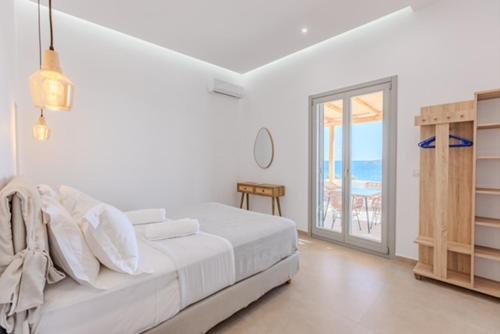 a white bedroom with a bed and a view of the ocean at Lipsi Grand Villas in Leipsoi