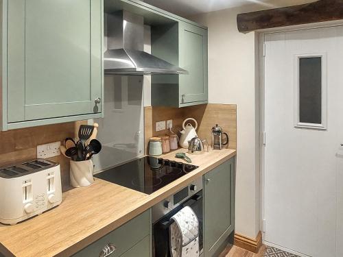a kitchen with green cabinets and a stove top oven at 13 Doomgate Cottage - Uk45056 in Appleby