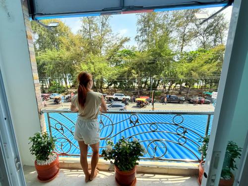 a woman standing on a balcony looking out of a window at Coastal Nomad Ocean View Stay - 1 or 2 Rooms in Ban Pak Khlong Phe