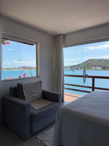 a bedroom with a bed and a chair and a large window at Villa Orion in Arraial do Cabo
