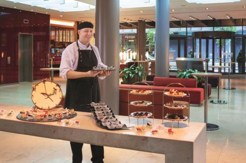 a man is holding a tray of food in a lobby at Mövenpick Hotel Frankfurt City Messe in Frankfurt/Main