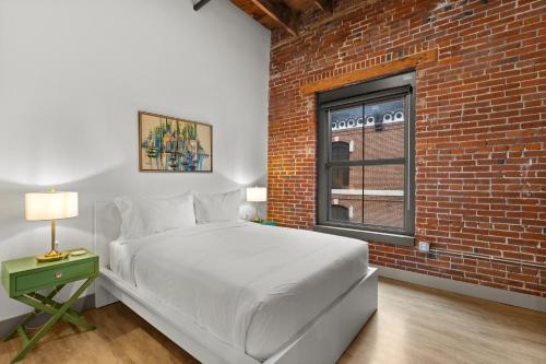 a bedroom with a white bed and a brick wall at Brick & Bed Riverfront Lofts, T 305 in Saint Louis