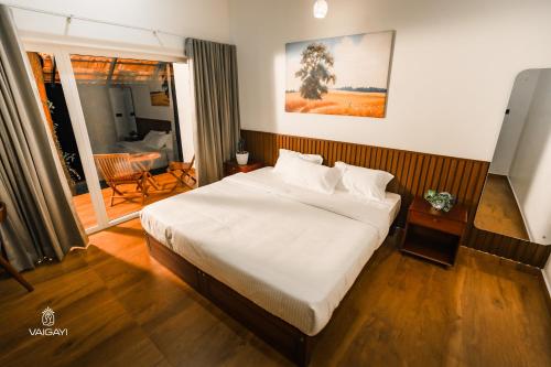 a bedroom with a large white bed and a balcony at Vaigayi Ayurveda and Yoga Resort in Kodanad
