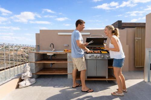a man and woman cooking food in a grill on a balcony at Villa Trilux, Infinity Pool, Jacuzzi, BBQ in Salobre