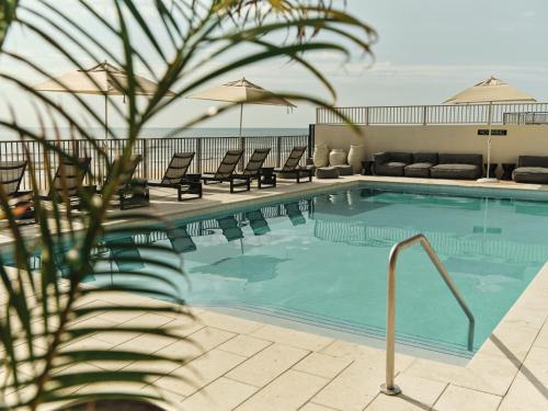 a swimming pool with chaise lounge chairs and the ocean at Ambros Daytona, Trademark Collection by Wyndham in Daytona Beach