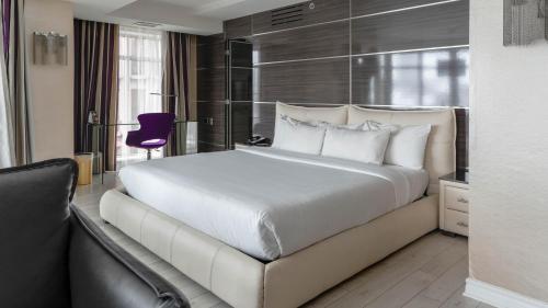 a bedroom with a large white bed and a purple chair at Hôtel Palace Royal Centre-Ville Québec par JARO in Quebec City