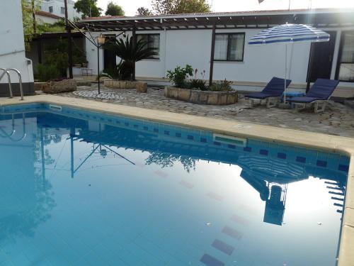 a swimming pool with an umbrella and chairs and a house at Hidden Cottage in Kyrenia
