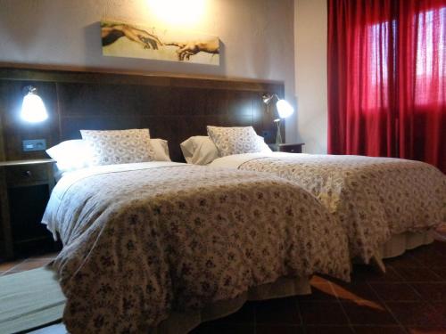 2 camas en una habitación de hotel con cortinas rojas en La Majada de la Covatilla, en La Hoya