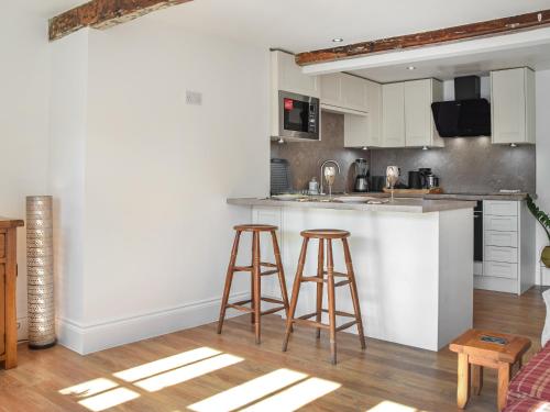 a kitchen with white cabinets and two bar stools at Kestrel Cottage in Holmfirth