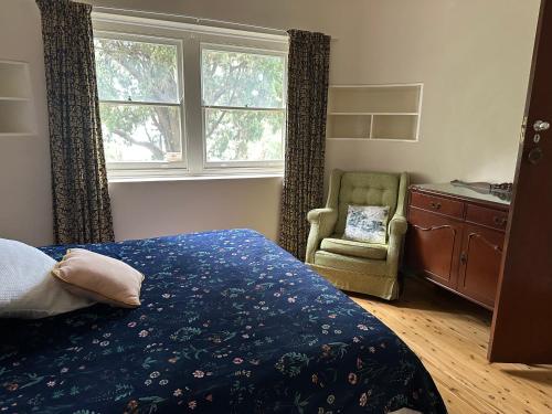 a bedroom with a bed and a chair and a window at Gracious 1930s Art Deco House in Gosford