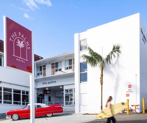 a red car parked in front of a building with a palm tree at The Palms Motel- Formerly Flinders Motel in Wollongong