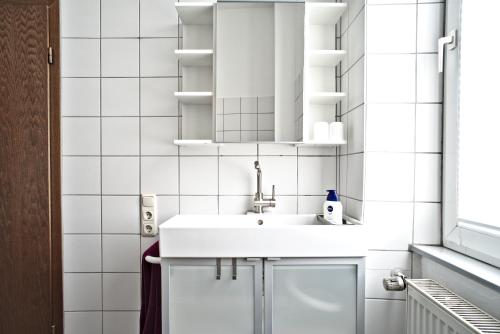 baño con lavabo y paredes de azulejos blancos. en City Apartment Mendig, en Mendig