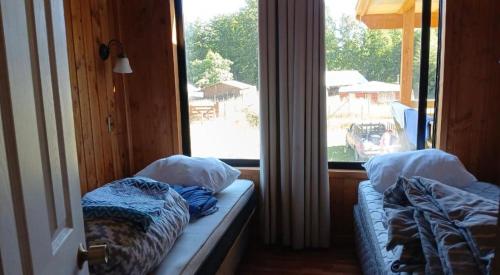 two beds in a room with a large window at Casa cerca de lago Caburgua in Pucón