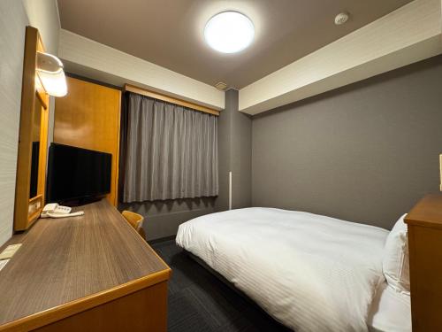 a hotel room with a bed and a desk with a television at Hotel Route-Inn Nakatsugawa Inter in Nakatsugawa